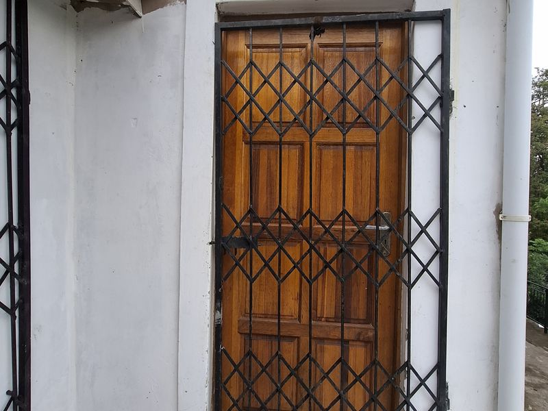Exterior view of a rear entrance featuring a timber door protected by a black metal security gate, set against a tiled patio area.