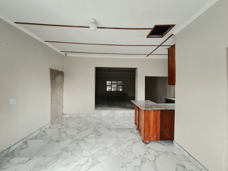 An open-plan living and kitchen area featuring marble-look floor tiles, wooden cabinetry, and a granite breakfast bar, currently awaiting final finishing touches.