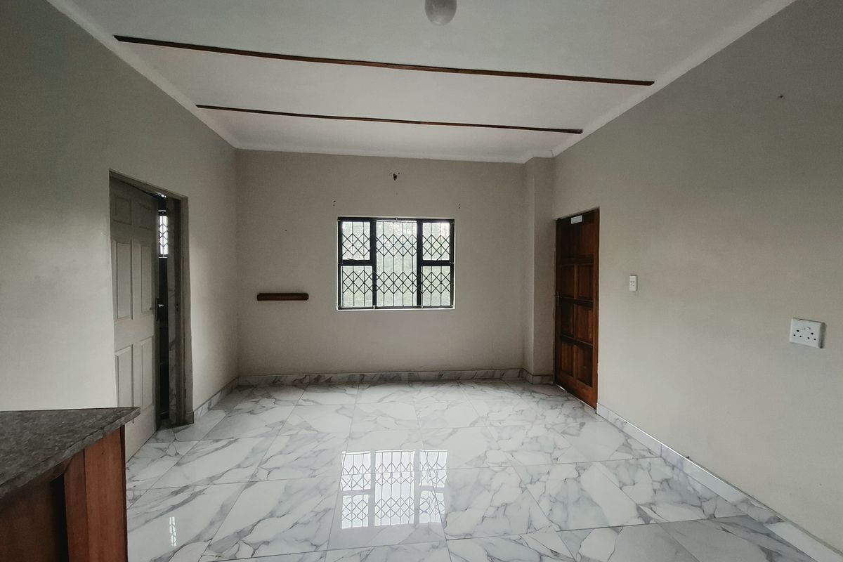 A bright, empty living area featuring modern marble-look floor tiles, decorative ceiling beams, and secure window bars.