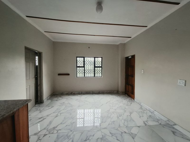 A bright, empty living area featuring modern marble-look floor tiles, decorative ceiling beams, and secure window bars.
