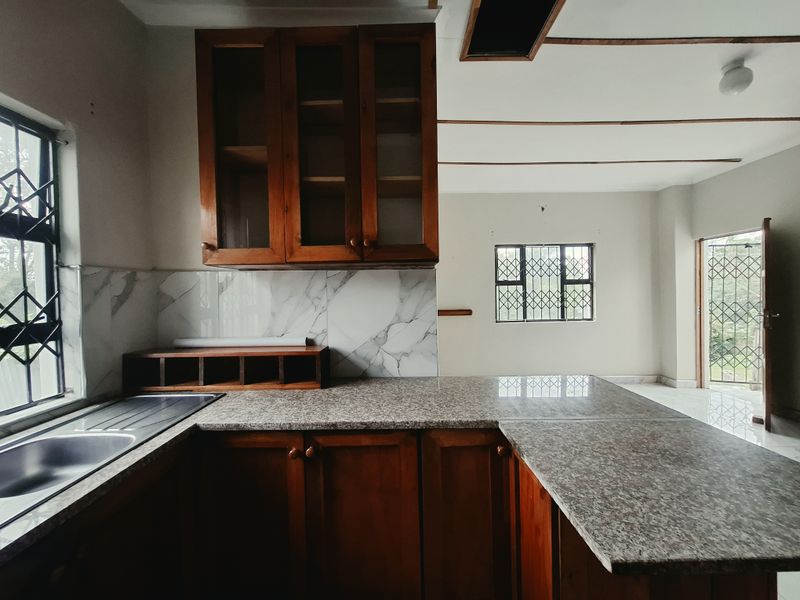 A functional kitchen featuring wooden cabinetry, granite countertops, and a marble-look splashback, with an open-plan layout leading to an adjacent living area.