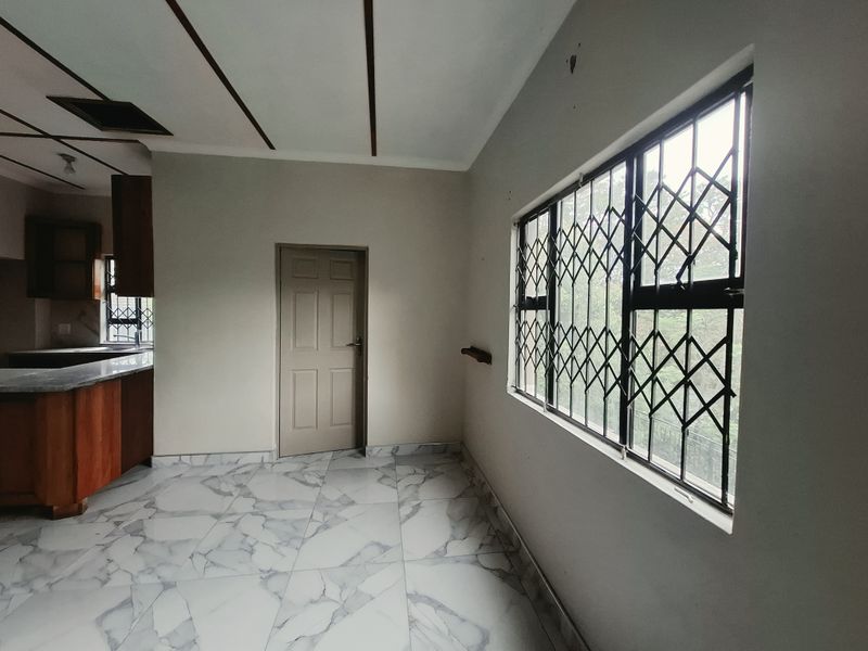 An open-plan living and kitchen area featuring marble-look floor tiles, security window bars, and built-in wooden cabinetry in the adjacent kitchen space.