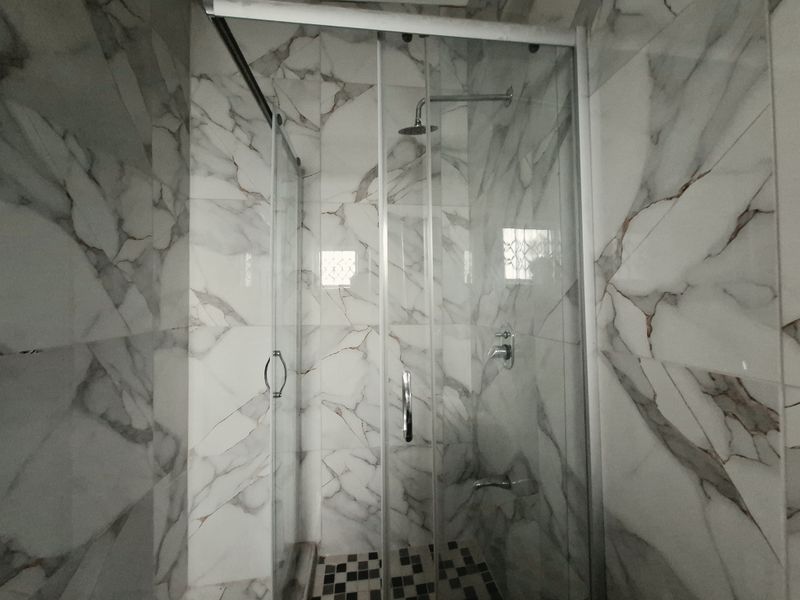 A modern bathroom shower featuring marble-effect wall tiles and a glass enclosure with chrome fixtures.
