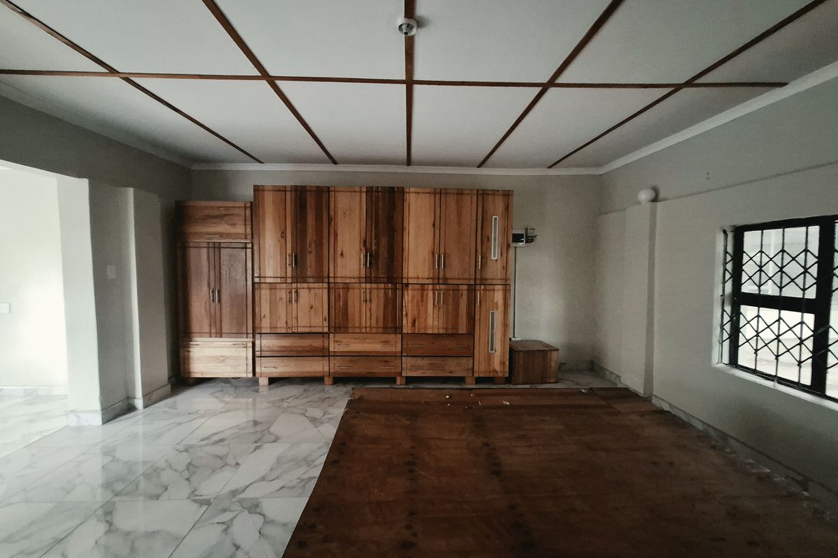 Spacious bedroom featuring extensive built-in wooden cabinetry, marble-look tiled flooring, and a distinctive wooden grid ceiling design.