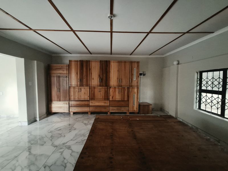 Spacious bedroom featuring extensive built-in wooden cabinetry, marble-look tiled flooring, and a distinctive wooden grid ceiling design.