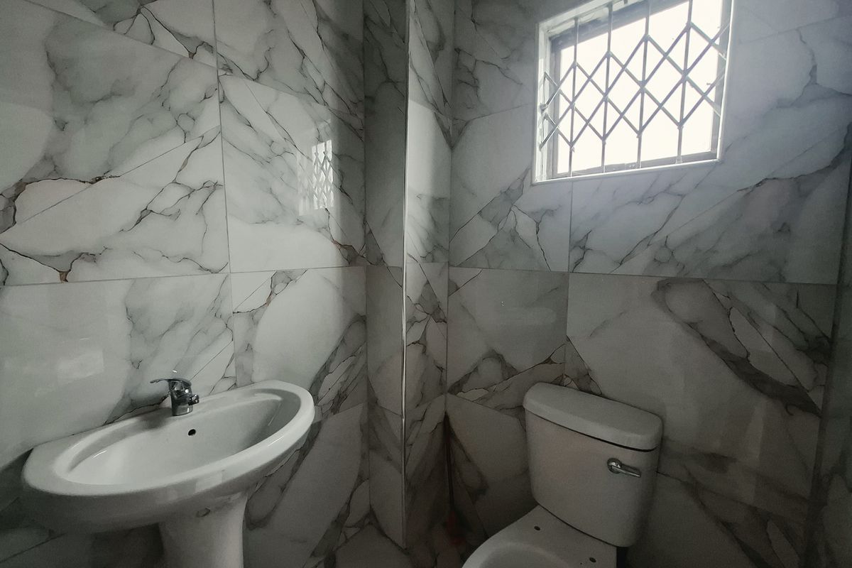 A modern bathroom featuring marble-effect wall tiling, a pedestal washbasin, and a standard toilet with security bars on the window.