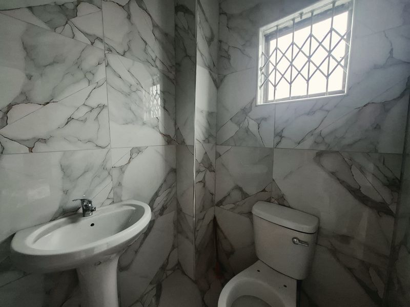 A modern bathroom featuring marble-effect wall tiling, a pedestal washbasin, and a standard toilet with security bars on the window.