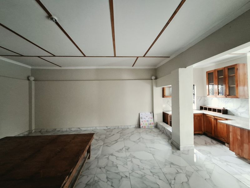 Spacious open-plan living and kitchen area featuring marble-look tiled flooring, wooden cabinetry, and a distinctive coffered ceiling design.