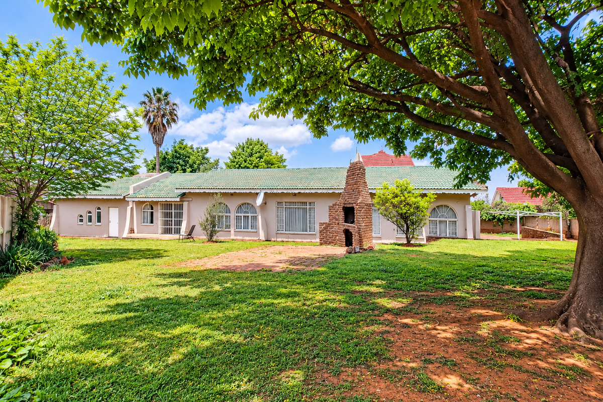 Spacious rear garden featuring a large mature tree, a brick built-in braai, and a paved patio area leading to the main house structure.