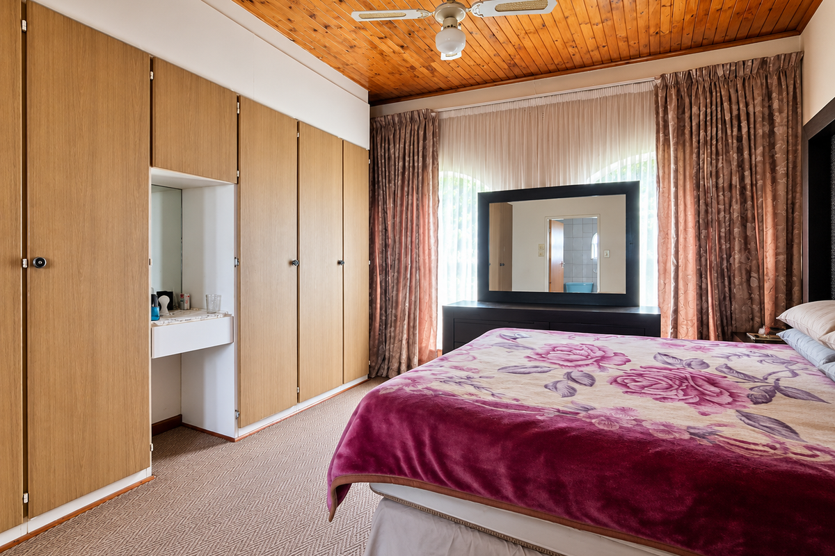 A bedroom featuring extensive built-in wooden cupboards with an integrated vanity, a warm timber-paneled ceiling, and a ceiling fan.