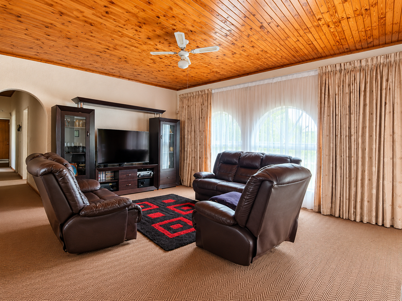A spacious living room featuring a warm timber tongue and groove ceiling, arched windows with floor-to-ceiling curtains, and a classic archway entrance.