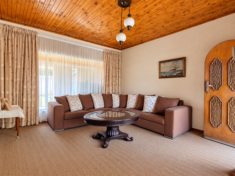 A cozy living room featuring a warm timber tongue and groove ceiling, textured walls, and a distinctive ornate wooden door.