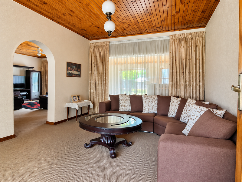A comfortable living room featuring a warm timber tongue and groove ceiling, an arched entryway, and large windows allowing for natural light.
