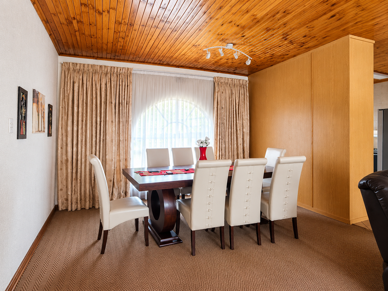 A dining room featuring a warm timber tongue and groove ceiling, built-in cabinetry, and a distinctive arched window with floor-to-ceiling curtains.