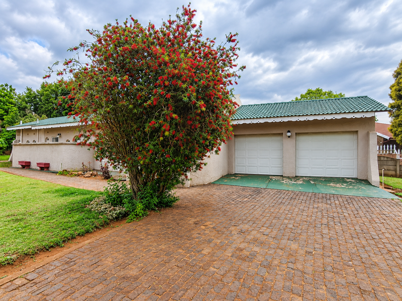Front view of a residential property featuring a double garage, brick paved driveway, and established garden with a large flowering tree.