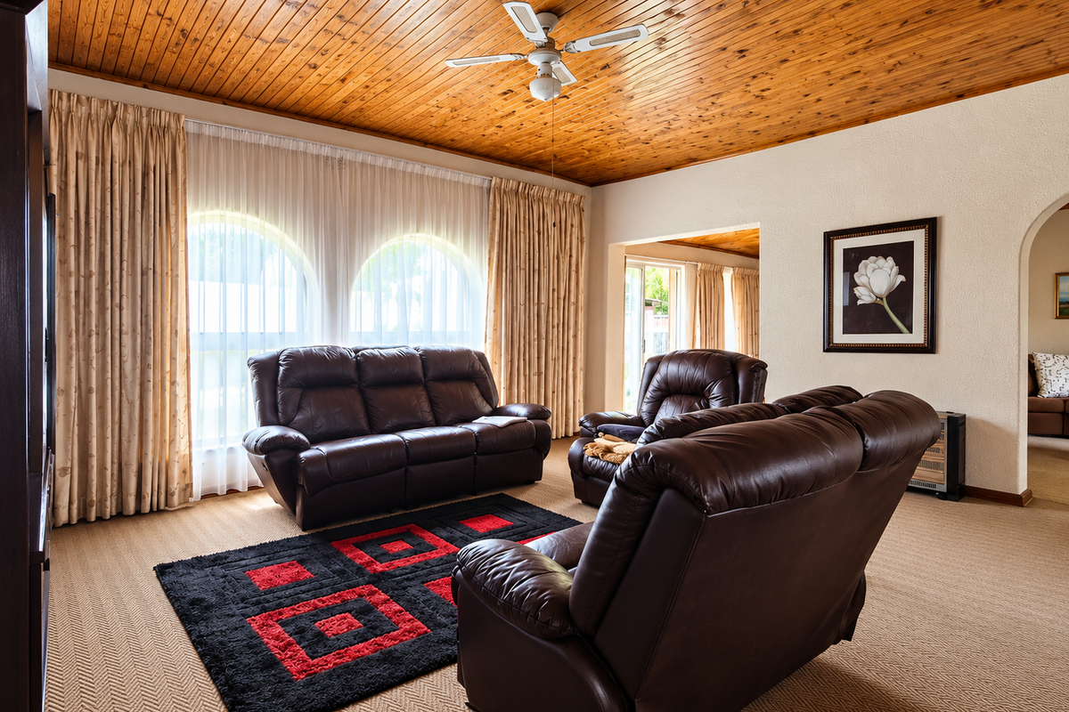 Spacious living room featuring a warm timber tongue and groove ceiling, ceiling fan, and distinctive arched windows with neutral carpeting.