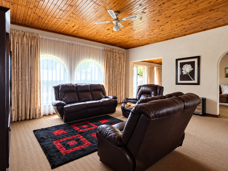 Spacious living room featuring a warm timber tongue and groove ceiling, ceiling fan, and distinctive arched windows with neutral carpeting.
