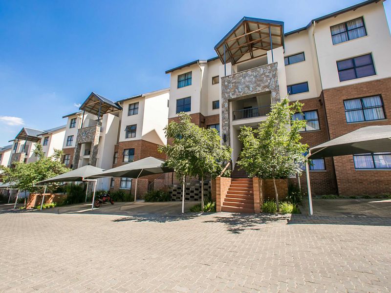 Front elevation of a multi-story apartment complex featuring brick and stone facade, paved driveway, and covered parking bays.