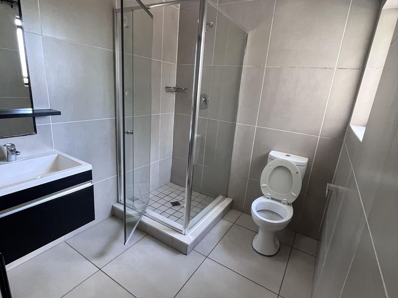 Modern bathroom featuring a glass shower enclosure, wall-mounted vanity with basin, and neutral floor-to-ceiling tiling.