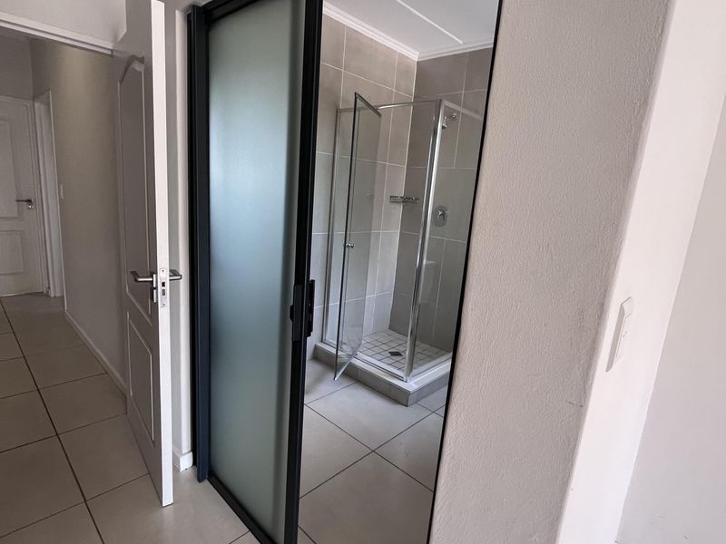 A modern bathroom featuring a glass-enclosed shower, neutral wall and floor tiling, and a sleek sliding door entry.