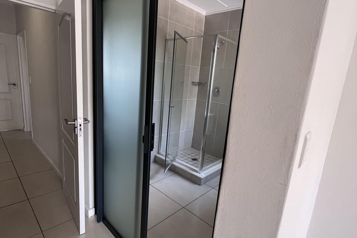 A modern bathroom featuring a glass-enclosed shower, neutral wall and floor tiling, and a sleek sliding door entry.