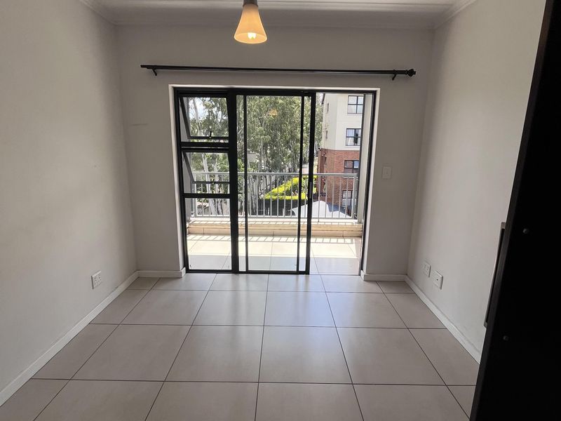 A bright, empty living area featuring neutral tiled flooring, a modern pendant light, and direct access to a private balcony through sliding glass doors.