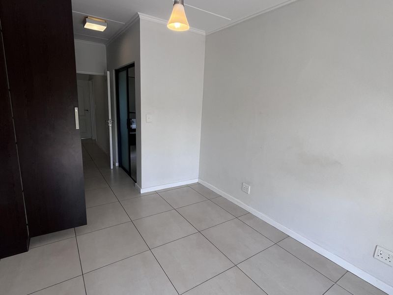 An empty bedroom featuring neutral tiled flooring, a built-in cupboard, and modern pendant lighting, offering a clean and versatile space.