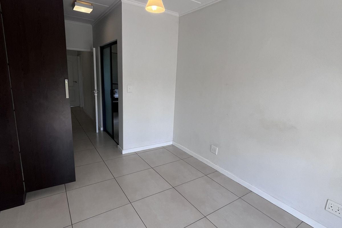 An empty bedroom featuring neutral tiled flooring, a built-in cupboard, and modern pendant lighting, offering a clean and versatile space.