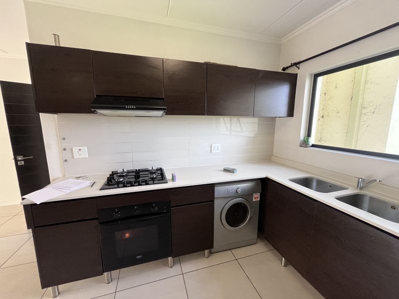 Modern kitchen featuring dark wood cabinetry, gas hob, built-in oven, extractor fan, and integrated washing machine with tiled flooring and backsplash.