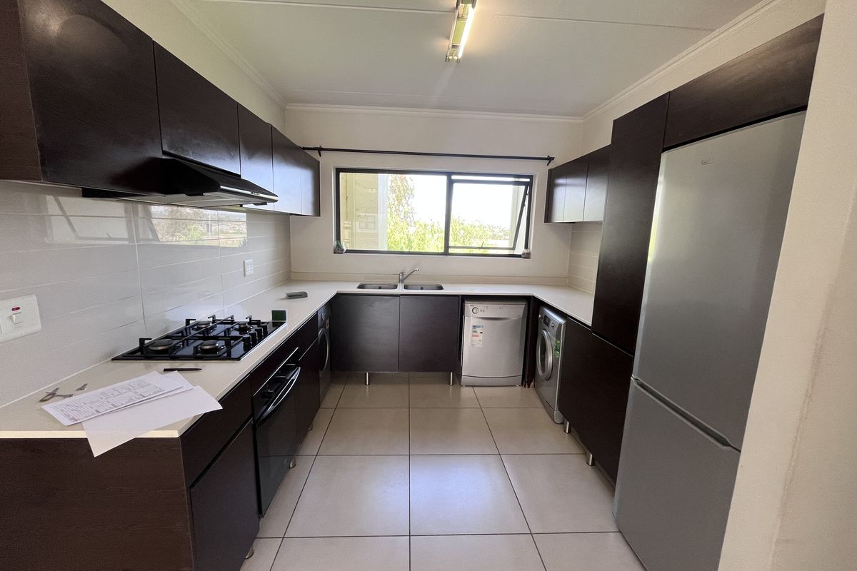 A functional kitchen featuring dark built-in cabinetry, a gas hob with extractor fan, double sink, and tiled flooring with a neutral backsplash.
