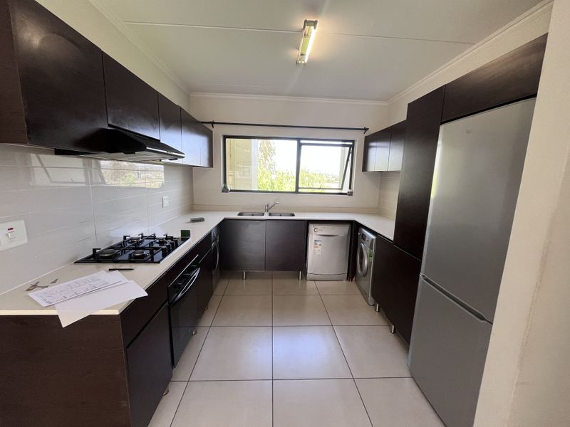 A functional kitchen featuring dark built-in cabinetry, a gas hob with extractor fan, double sink, and tiled flooring with a neutral backsplash.