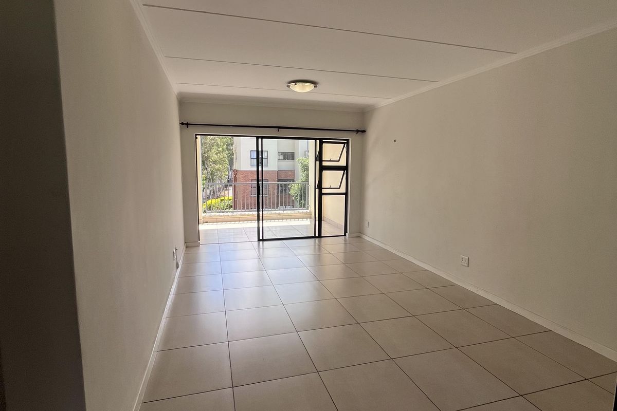 A bright, empty living room featuring neutral tiled flooring and a sliding glass door that opens onto a balcony.