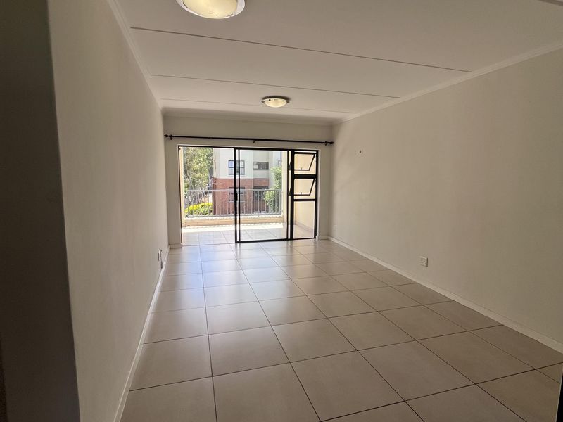 A bright, empty living room featuring neutral tiled flooring and a sliding glass door that opens onto a balcony.