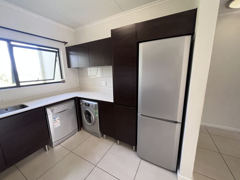 A modern kitchen featuring dark wood cabinetry, white stone countertops, tiled flooring, and dedicated spaces for a dishwasher and washing machine.