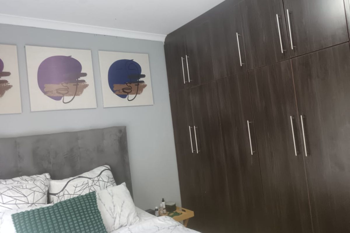 A bedroom featuring dark wood built-in cupboards with modern metal handles and neutral wall finishes.