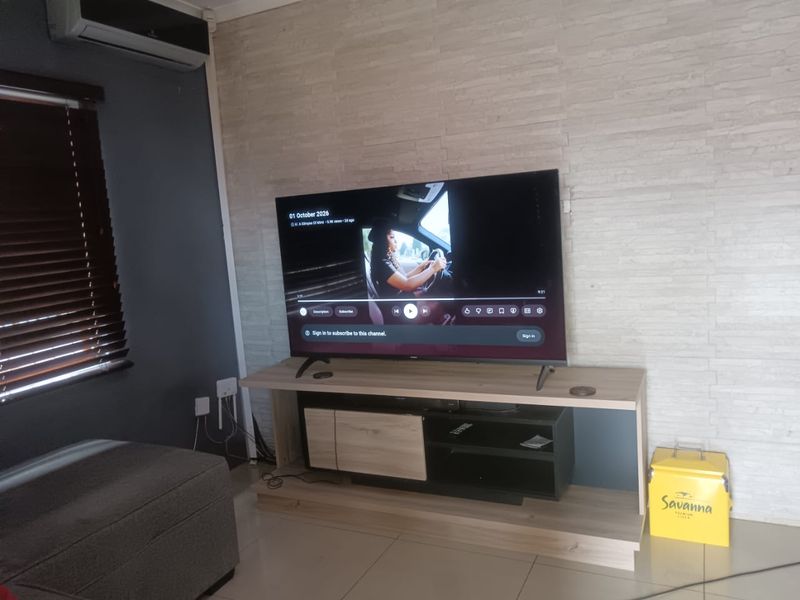 A living room featuring a textured stone-cladding accent wall, tiled flooring, and a wall-mounted air conditioning unit.