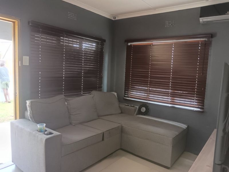 A comfortable living room featuring tiled flooring, dark grey walls, wooden venetian blinds, and a wall-mounted air conditioning unit.