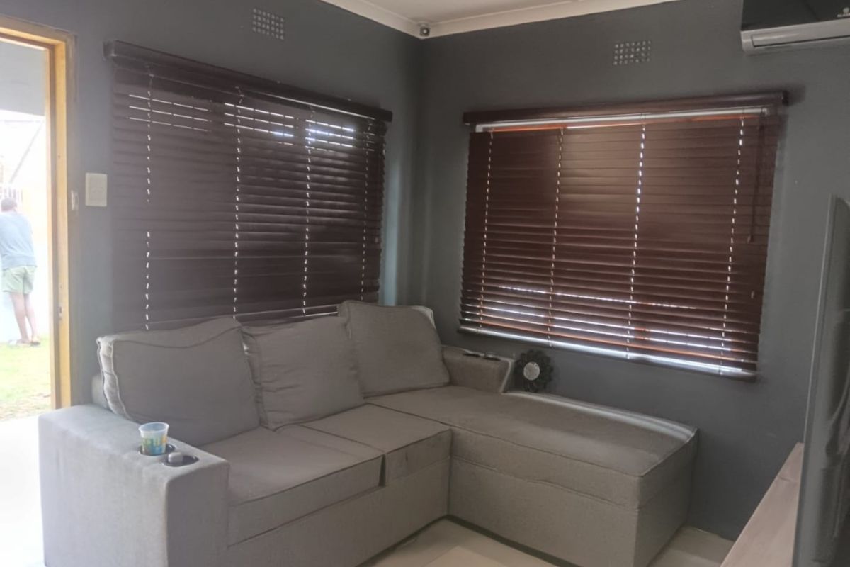 A comfortable living room featuring tiled flooring, dark grey walls, wooden venetian blinds, and a wall-mounted air conditioning unit.
