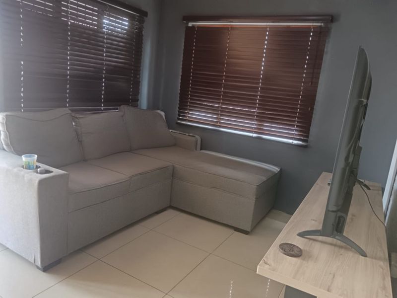 A cozy living room featuring neutral tiled flooring and dark wood-style venetian blinds, providing a functional and private space.