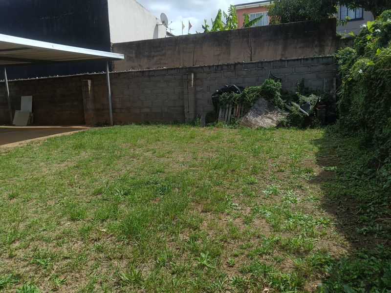 A rear garden area featuring a concrete block boundary wall and a metal carport structure, currently requiring landscaping and maintenance.