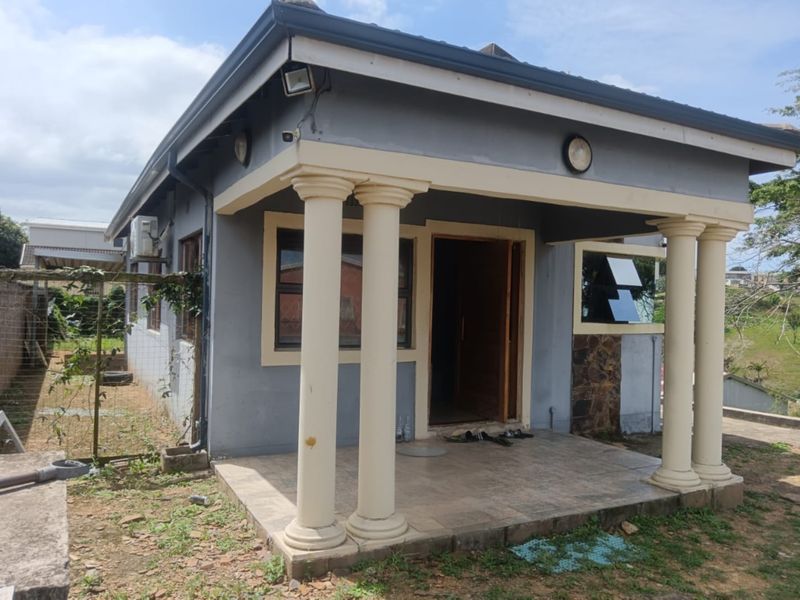 Front elevation of a house featuring a covered patio with classical columns, stone cladding accents, and an external air conditioning unit.
