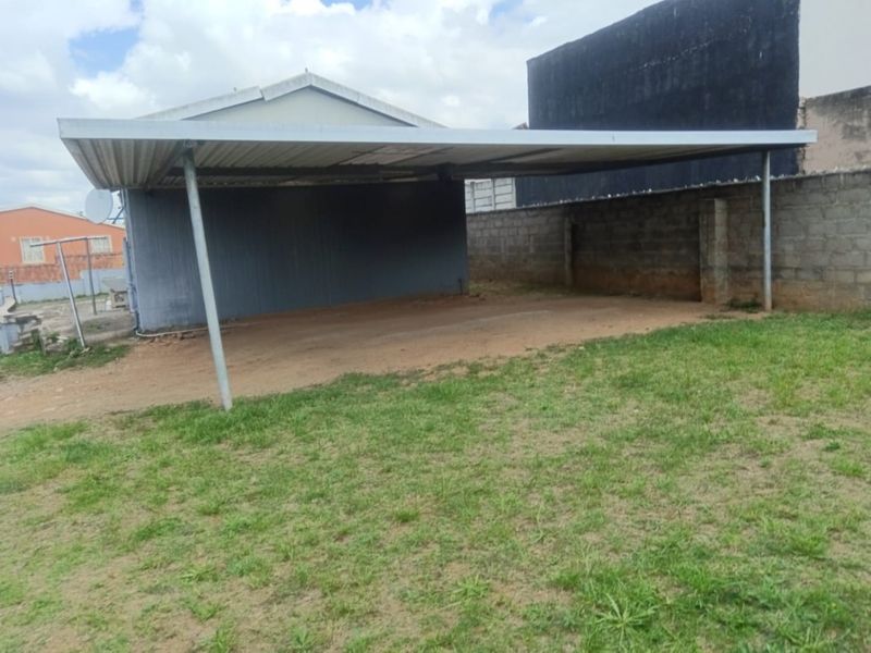 A functional metal carport structure providing covered parking space, situated on an unpaved area with adjacent boundary walling.
