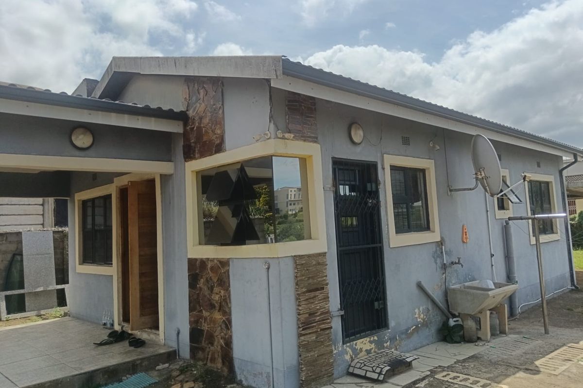 Rear view of the house featuring a covered patio area, stone cladding accents, and an external wash basin with visible wear to the exterior paint.