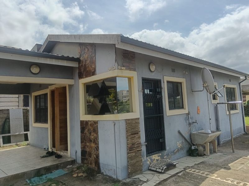 Rear view of the house featuring a covered patio area, stone cladding accents, and an external wash basin with visible wear to the exterior paint.