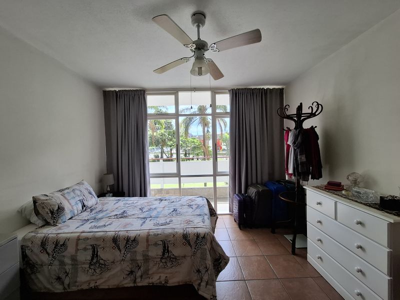 A bedroom featuring tiled flooring, a ceiling fan, and a large window with access to a balcony, providing natural light and ventilation.