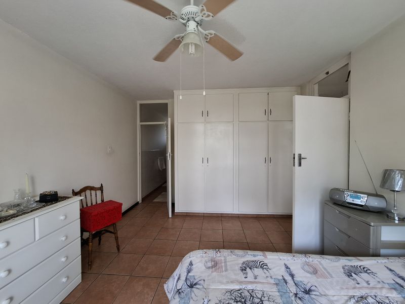 A bedroom featuring tiled flooring, a ceiling fan, and ample built-in cupboard storage, with an adjoining doorway leading to another room.