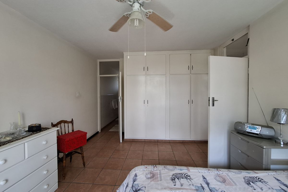 A bedroom featuring tiled flooring, a ceiling fan, and ample built-in cupboard storage, with an adjoining doorway leading to another room.