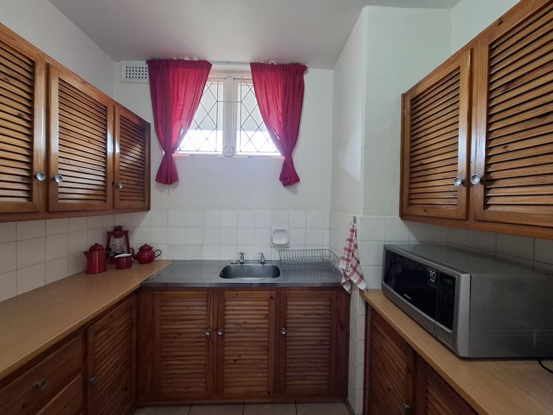 A functional kitchen featuring wooden louvered cabinetry, a stainless steel sink, tiled backsplash, and a built-in microwave.