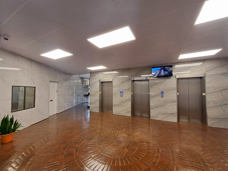 A spacious apartment building lobby featuring marble-look wall finishes, circular brick flooring, and three elevator access points.