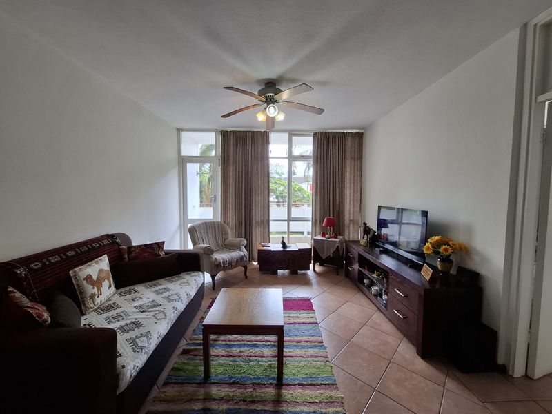 A living room featuring tiled flooring, a ceiling fan, and a sliding glass door providing access to an outdoor area.